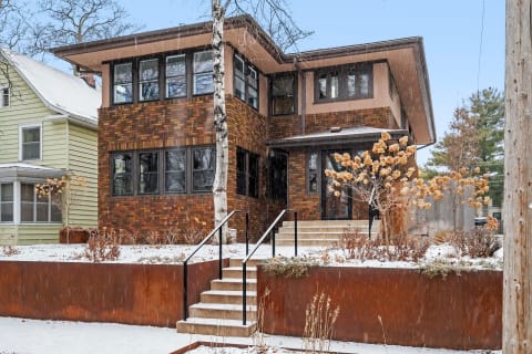 Modern two-story home made of brick with winter landscape featuring snow and dried plants.