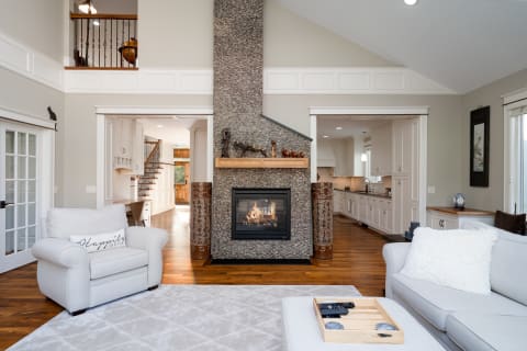 Modern living room with a stone fireplace, gray furniture, and wooden accents.