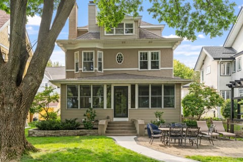 A beautiful two-story house with a porch, large windows, and outdoor patio furniture.