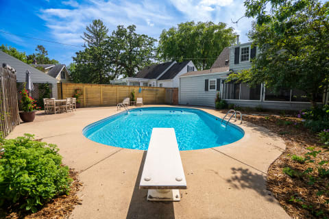 A backyard with a swimming pool, diving board, and dining set under a blue sky.