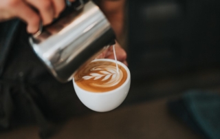 Close up of person pouring milk into a latte mug.